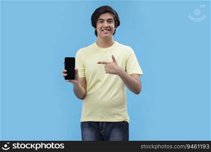 Portrait of a teenage boy showing Smartphone while standing against blue background