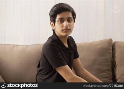 PORTRAIT OF A TEENAGE BOY SITTING AND LOOKING AT CAMERA