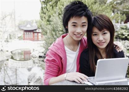 Portrait of a teenage boy sitting with his arm around a young woman using a laptop