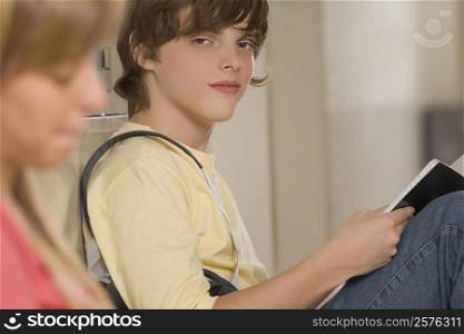 Portrait of a teenage boy studying with his friend sitting beside her