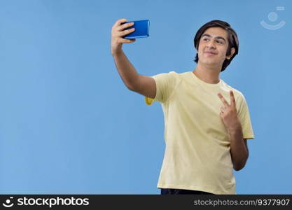 Portrait of a teenage boy taking selfie on Smartphone while standing against blue background