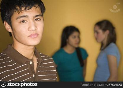 Portrait of a teenage boy with two teenage girls talking in the background