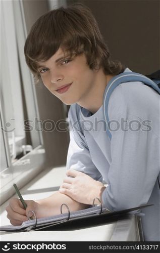 Portrait of a teenage boy writing on spiral notebook and smiling