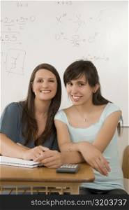Portrait of a teenage girl and a female teacher sitting in a classroom and smiling