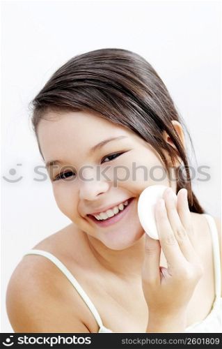 Portrait of a teenage girl applying face powder on her cheeks