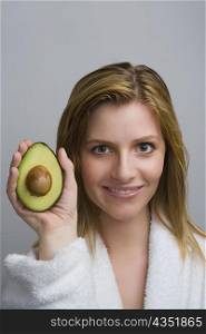 Portrait of a teenage girl holding a half of avocado and smiling