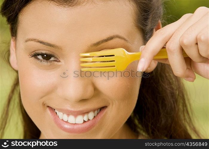 Portrait of a teenage girl holding a plastic fork in front of her eye