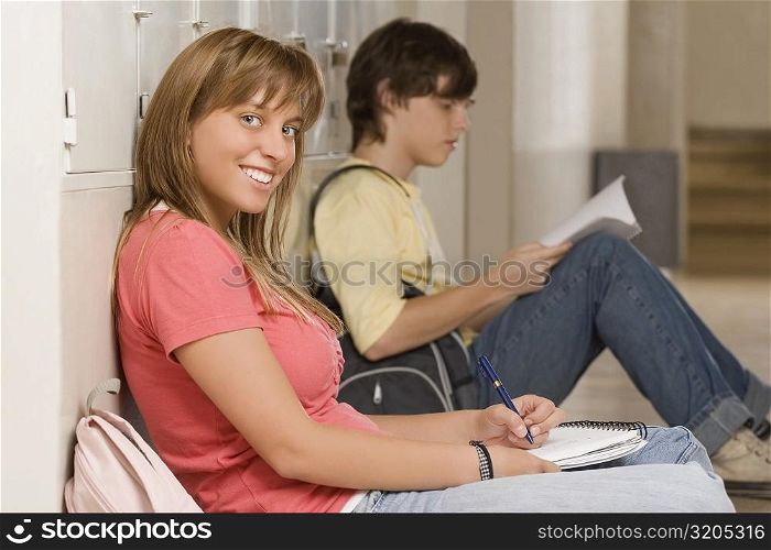 Portrait of a teenage girl leaning against a wall and studying with a teenage boy beside her