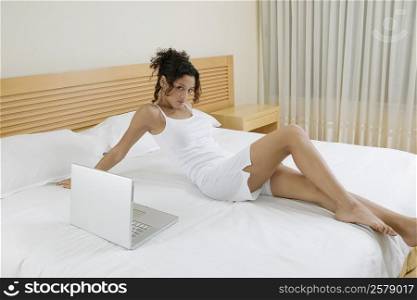 Portrait of a teenage girl reclining on the bed beside a laptop