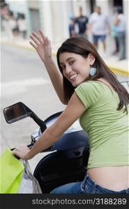 Portrait of a teenage girl riding on a scooter and waving her hand