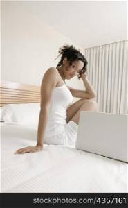 Portrait of a teenage girl sitting on the bed beside a laptop