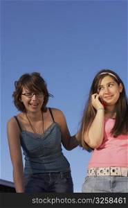 Portrait of a teenage girl smiling and her sister talking on a mobile phone