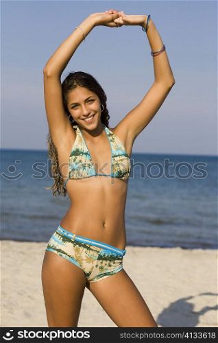 Portrait of a teenage girl standing on the beach with her arms raised