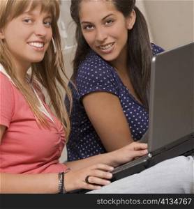 Portrait of a teenage girl using a laptop with her friend sitting beside her