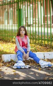 Portrait of a ten-year girl sits on a playground in roller skates