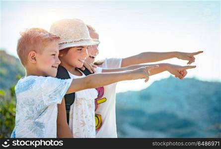 Portrait of a three happy friends outdoors, kids with wonder looking at the view, with excitement enjoying amazing mountains, best friends with pleasure spending summer holidays together. Happy little friends traveling together