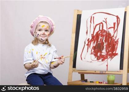 Portrait of a three-year old girl playing in the artist. Girl mud paints. Standing behind you easel