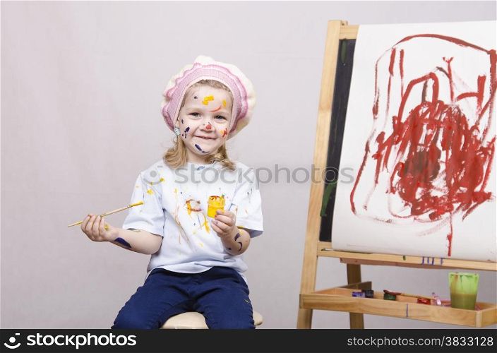 Portrait of a three-year old girl playing in the artist. Girl mud paints. Standing behind you easel