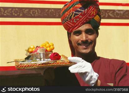 Portrait of a train steward holding winter cherries and a Rose flower on a serving tray, India