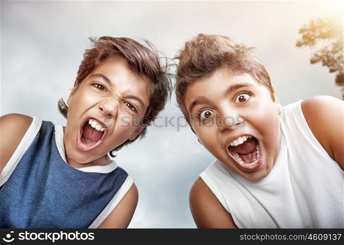 Portrait of a two crazy boys screaming to camera, over grey sky background, allow to enjoy the pleasure of freedom in a summer camp&#xA;