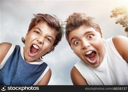 Portrait of a two crazy boys screaming to camera, over grey sky background, allow to enjoy the pleasure of freedom in a summer camp&#xA;