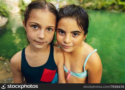 Portrait of a two cute little girls standing near the mountain’s lake, with pleasure spending time in summer c&, happy best friends enjoying summer time together