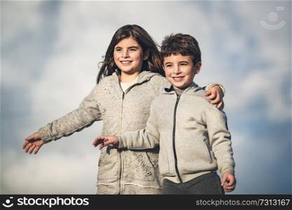 Portrait of a two happy children over sky background, little brother and sister having fun together outdoors in spring day