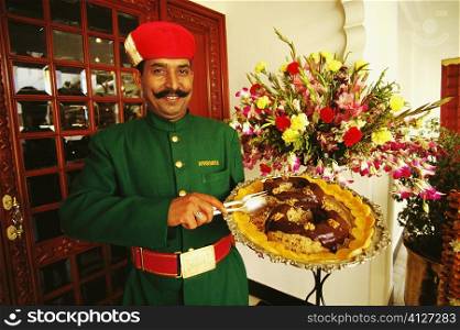 Portrait of a waiter holding a dish plate and smiling, Lake Palace, Udaipur, Rajasthan, India