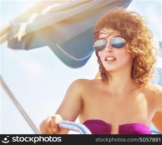 Portrait of a woman driving sailboat, female wearing stylish sunglasses and swimsuit posing at the helm, enjoying summer vacation