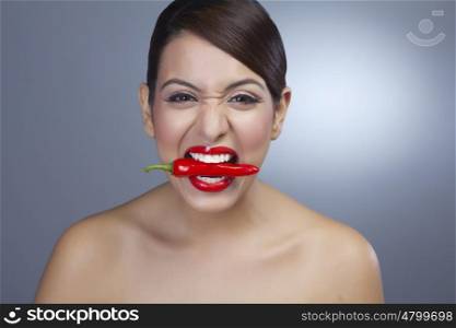 Portrait of a woman holding red pepper in teeth