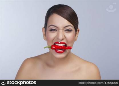 Portrait of a woman holding red pepper in teeth