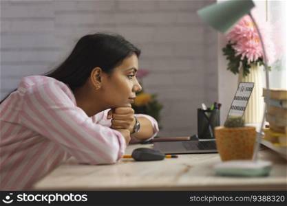 Portrait of a woman looking at laptop with resting her chin on desk 