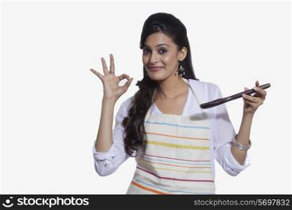 Portrait of a woman with a cooking utensil giving ok sign