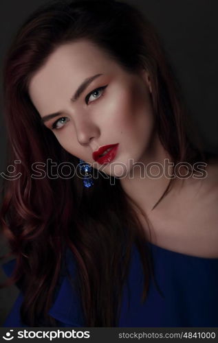 Portrait of a woman with professional makeup. Blue dress and earrings, close-up face.