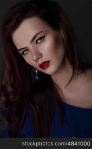 Portrait of a woman with professional makeup. Blue dress and earrings, close-up face.