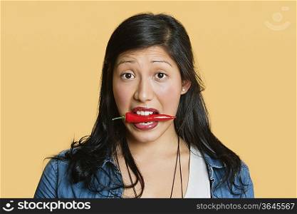 Portrait of a woman with red chili pepper in mouth over colored background
