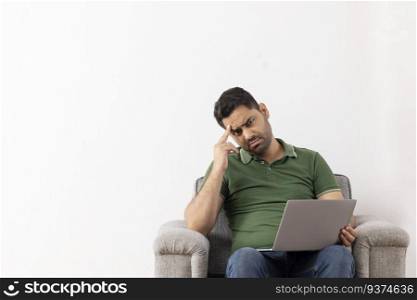 Portrait of a worried young man sitting on sofa with laptop on his lap
