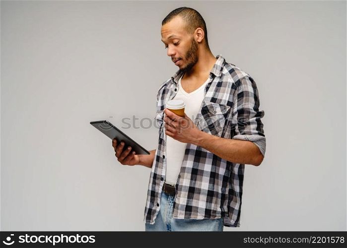 Portrait of a young african american man wearing casual shirt holding tablet pc pad and cup of coffee.. Portrait of a young african american man wearing casual shirt holding tablet pc pad and cup of coffee