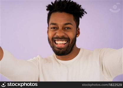 Portrait of a young afro man looking at camera and smiling while taking a selfie against isolated background.