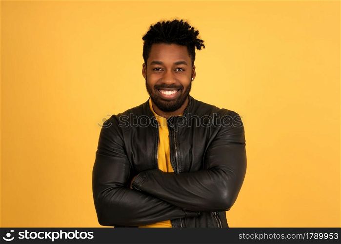Portrait of a young afro man looking at the camera and smiling while standing against isolated yellow background.