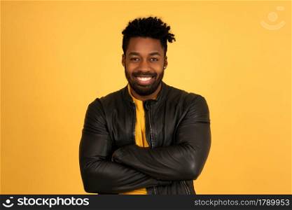 Portrait of a young afro man looking at the camera and smiling while standing against isolated yellow background.