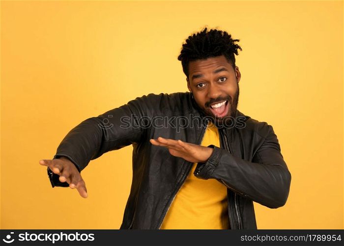 Portrait of a young afro man looking happy and excited while standing against isolated yellow background.