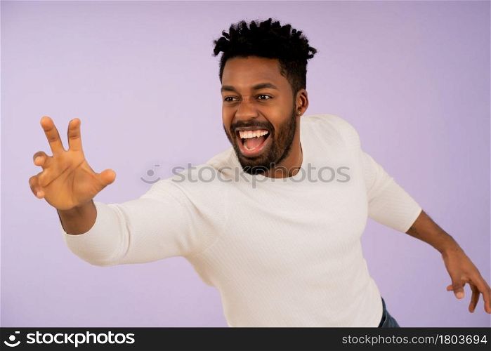 Portrait of a young afro man smiling while trying to catch something with his hand against isolated background.