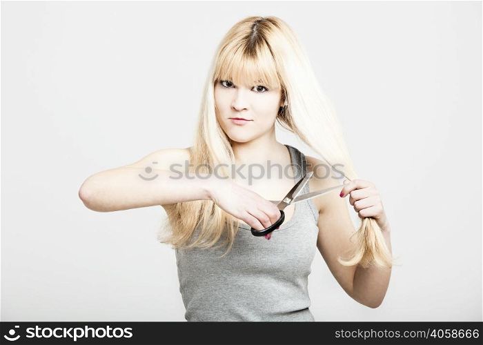 Portrait of a young and beautiful blonde cutting her own hair