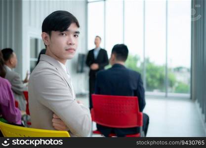 Portrait of a young Asian businessman sitting behind a seminar room with a colleague in the foreground listening to the lecture