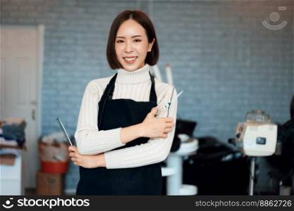 Portrait of a young asian female hairdresser holding qualified haircut tools in her salon for a woman&rsquo;s haircut. Photo job concept for small business owner and haircare.. Portrait of a young asian female hairdresser holding qualified haircut tools.