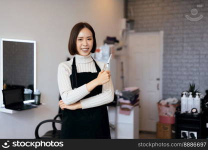 Portrait of a young asian female hairdresser holding qualified haircut tools in her salon for a woman’s haircut. Photo job concept for small business owner and haircare.. Portrait of a young asian female hairdresser holding qualified haircut tools.