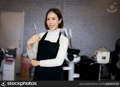 Portrait of a young asian female hairdresser holding qualified haircut tools in her salon for a woman’s haircut. Photo job concept for small business owner and haircare.. Portrait of a young asian female hairdresser holding qualified haircut tools.