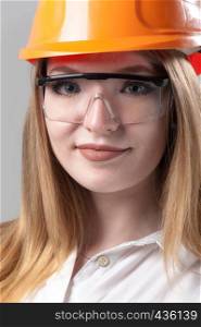 Portrait of a young attractive woman with blond hair in orange helmet and glasses on a neutral gray background.. Portrait of a young attractive woman with blond hair in orange helmet on a neutral gray background.