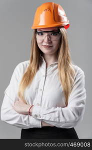 Portrait of a young attractive woman with blond hair in orange helmet and glasses on a neutral gray background.. Portrait of a young attractive woman with blond hair in orange helmet on a neutral gray background.